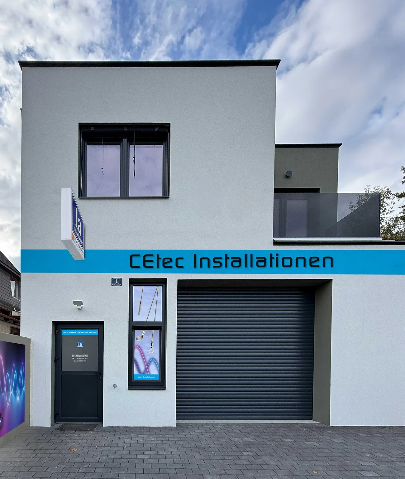 Firmenhaus von CEtec Installationen frontal: blaues Fassadenband mit Schriftzug, Leuchtschild und Eingangstür mit den Öffnungszeiten